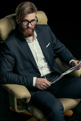 Stylish businessman in eyeglasses holding newspaper on black