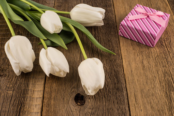 White tulips with gift on old wooden table.