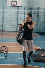Young sportsman with sports bottle and bag looking away in gym
