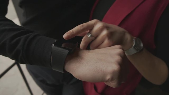 Close up shot on the hands of a young couple who check incoming messages on smart watches. Girl with neat manicure leads finger on the touch screen.