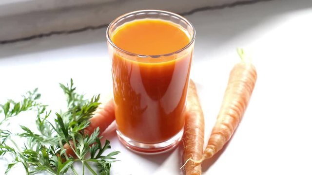 Handheld high key close up shot of a glass of carrot juice and some whole carrots that is a healthy choice for dietary nutrition.