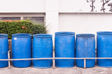 Big blue bins arrange next to building and plants.