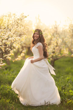 Portrait of the bride in ivory wedding dress with long curly hair walking in gardens with blossom trees like in fairy tale
