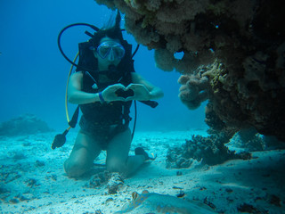Young female on the seafloor showing love signal to a small slope while diving