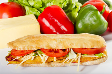 Fasting sandwich - Ciabatta with breaded peppers, tomatoes and vegetable cheese next to the fresh ingredients.