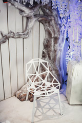 Original white chair made like a diamond stands before decorative grey tree