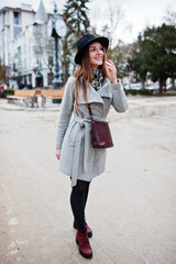 Young model tourist girl in a gray coat and black hat with leather handbag on shoulders posed at street of city.