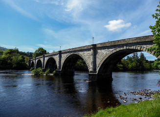Fototapeta na wymiar Old stone bridge spanning across river in countryside