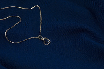 Fototapeta na wymiar Golden chain with pendant in form of heart on the deep blue background