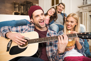 Group of happy young friends enjoying guitar at home