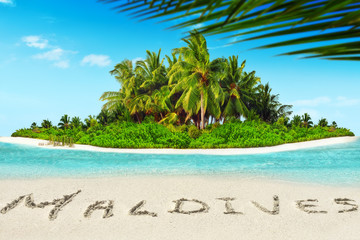 Whole tropical island within atoll in tropical Ocean and inscription "Maldives" in the sand on a tropical island,  Maldives.