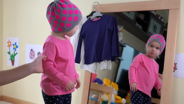 Woman and girl put hats on head near mirror
