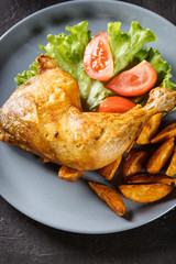 Roasted chicken legs with potato wedges and tomatoes