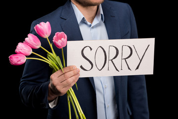 partial view of stylish man holding tulips bouquet and sorry sign on black