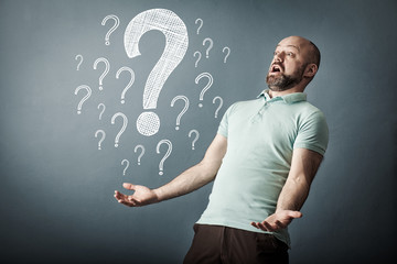 Happy bearded middle-aged man trying to find way to solve problem, with many question marks