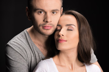 portrait of man looking to camera while hugging woman on black