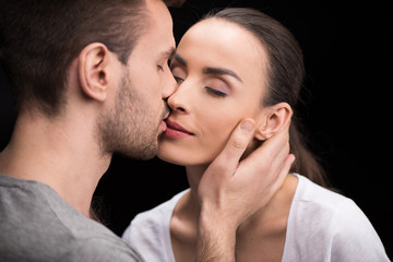portrait of man sensually kissing woman on black