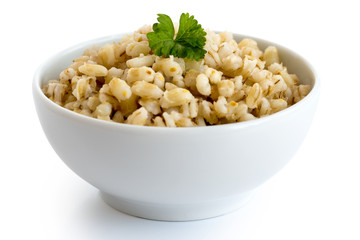 Cooked pearl barley with green parsley in white ceramic bowl isolated on white.