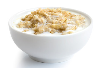 Cooked whole porridge oats with milk and brown sugar in white ceramic bowl isolated on white.