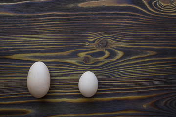 Two different size eggs on the dark wood background tell us that size matters