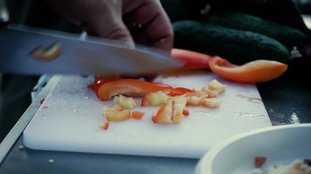 Cooking on the open fire. Male hands cutting red ripe bell pepper into small pieces on a cutting board. HD