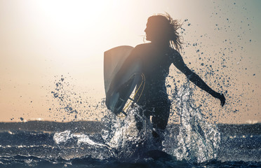 Woman smiles and runs into the sea with lots of splashes - obrazy, fototapety, plakaty