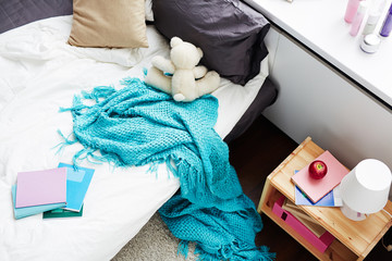 Unmade bed of girl with white lonely teddy bear and blue blanket hanging down on floor, high angle...