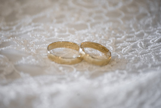 Two gold wedding rings on a white wedding dress
