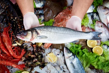 Photo sur Plexiglas Poisson Vendeur présentant un poisson de bar frais en poissonnerie