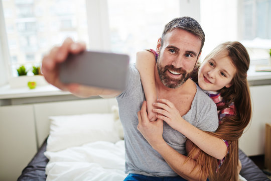 Beautiful Little Girl With Long Red Hair Hugging Her Joyful Bearded Dad And Posing For Selfie