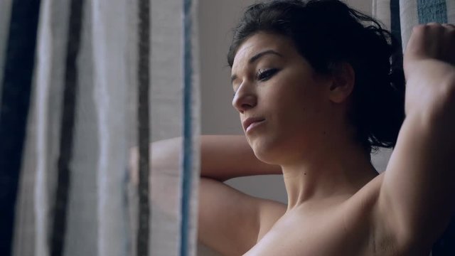 pensive, young brunette touching her hair at the window