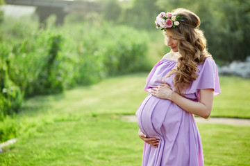 Pregnant woman walks in park at evening. Family enjoying pregnancy. The concept of Mother's Day and Women's Day.