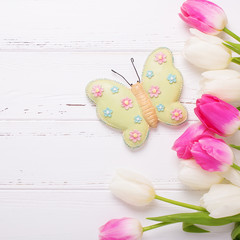 Bright pink and white tulips flowers and decorative butterfly  on  wooden background.