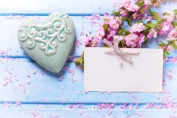 Pink sakura  flowers, empty tag  and  turquoise  decorative heart on blue wooden planks.