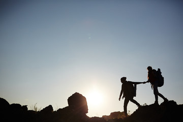 Wide shot side view image of backlit couple walking on mountain top against the sun