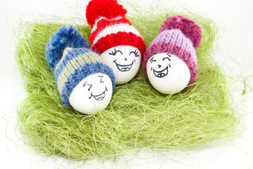 Easter eggs on green sisal. Emoticons in knitted hat with pom-poms. Handmade.