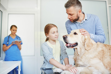 Father and daughter calming and petting their dog while waiting for medical examination at vet clinic