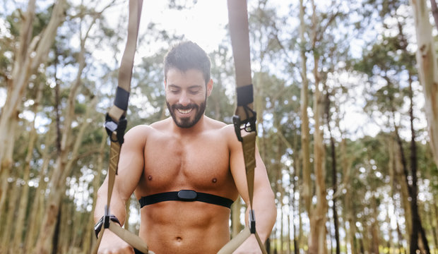 Smiling bare chested man doing suspension training outdoors