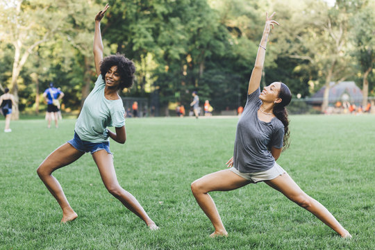 Two young women doing yoga exercise in a park