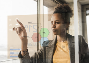 Young woman touching glass wall with data in office