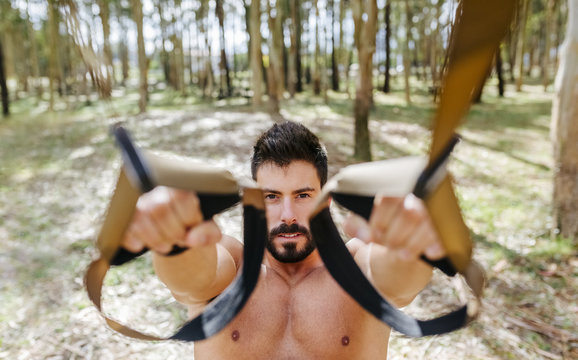 Bare chested man doing suspension training outdoors