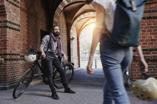 Man with electric bicycle watching passing woman