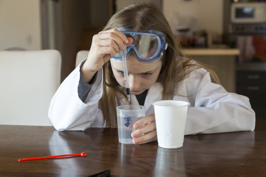 Girl wearing work coat and safety glasses using chemistry set at home