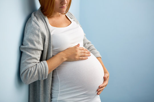 Mid-section image with focus on bog belly of gentle pregnant woman in blue room