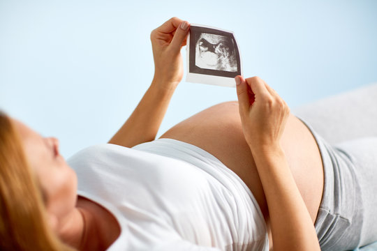 Pregnant woman lying on medical bench in doctors office and looking at black and white image of her baby from ultrasound scan