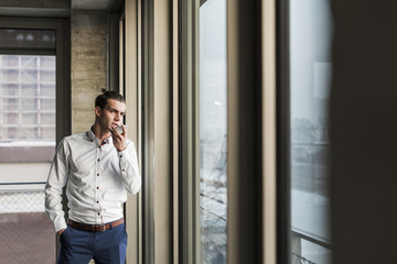 Young businessman using cell phone at the window