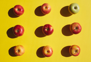 Directly above view of ripe red apples arranged in rows, with one green apple standing out,  on bright yellow background, healthy eating concept
