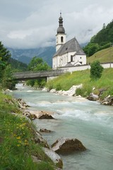 Fototapeta na wymiar Parish church of Saint Sebastian in Ramsau, Germany with the Bavarian Alps in the background and the river Ramsauer Ache in the foreground. Built in 1512