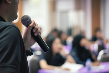 A teacher is holding microphone in his hand and teaching students in classroom in selective focus...