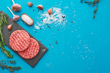 Fresh raw beef meat with herbs and salt on turquoise background. Flat lay.